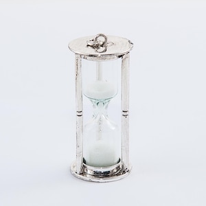 May include: A silver hourglass with white sand inside. The hourglass has a circular top and base, with a decorative metal frame. The sand timer is a classic design, suitable for home decor or as a functional item.
