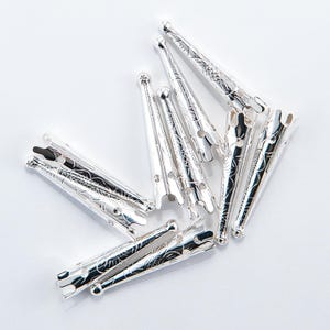 May include: A group of silver-colored metal tips with an ornate design. The tips are pointed and have a small hole at the top.