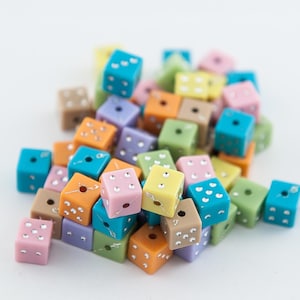 May include: A pile of colorful dice beads in various pastel colors, including pink, blue, green, yellow, and orange. The dice have silver dots on each side.