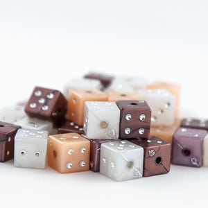 May include: A pile of small, colorful dice with white, brown, and beige colors. The dice are made of plastic and have a glossy finish.