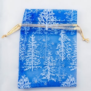 Puede incluir: Una bolsa de regalo de malla azul con un patrón de copo de nieve blanco y una cinta dorada.