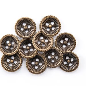 May include: A collection of bronze-colored buttons with a radial design. Each button features four holes and a decorative pattern of lines radiating from the center. The buttons are arranged on a white background.