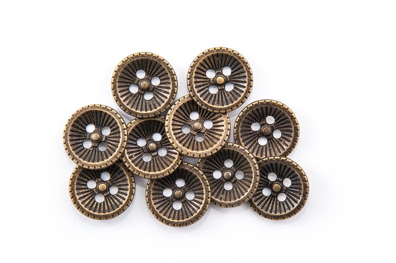 May include: A collection of bronze-colored buttons with a radial design. Each button features four holes and a decorative pattern of lines radiating from the center. The buttons are arranged on a white background.