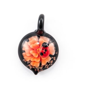 May include: A black glass pendant with a red ladybug on a pink flower. The pendant has gold glitter accents.