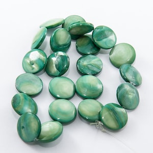 Peut inclure: Un collier de perles rondes et plates en nacre verte irisée. Chaque perle présente une surface lisse et polie avec des motifs tourbillonnants dans des tons vert émeraude clair et foncé, enfilées sur un fil de filament fin et transparent.