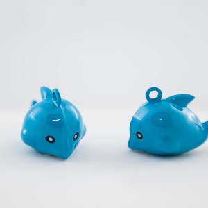 May include: Two blue plastic dolphin toys with black eyes and a white background.