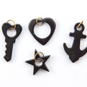May include: Four dark gray charms with gold-colored jump rings. The charms are shaped like a key, a heart, a star, and an anchor. The charms are displayed on a white background.