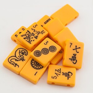 Puede incluir: Un conjunto de fichas de mahjong de color naranja con caracteres y s&iacute;mbolos chinos negros. Las fichas est&aacute;n dispuestas en una pila sobre una superficie blanca.
