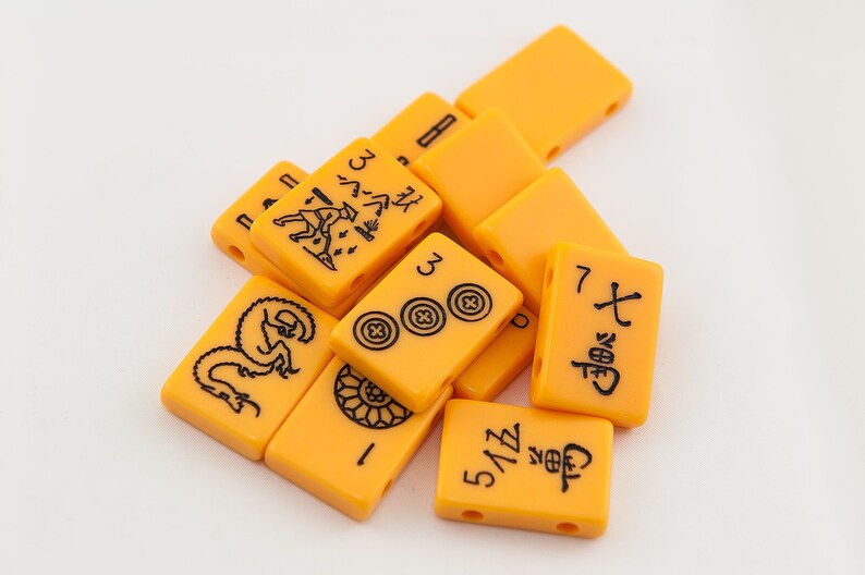 Puede incluir: Un conjunto de fichas de mahjong de color naranja con caracteres y s&iacute;mbolos chinos negros. Las fichas est&aacute;n dispuestas en una pila sobre una superficie blanca.