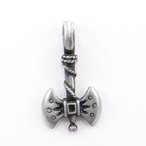 May include: A silver-colored axe pendant with a double-bladed head and a detailed handle. The handle is wrapped with a rope-like design. The axe head features decorative rivets and a square center. A small loop is at the top for a chain.