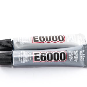 Puede incluir: Dos tubos de adhesivo de contacto industrial E6000. Los tubos son plateados con tapas negras y texto rojo y blanco. Un tubo contiene 5,3 ml.
