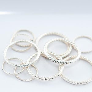 Peut inclure: Un ensemble d'anneaux en argent avec un design torsadé. Les anneaux sont disposés en pile sur une surface blanche.