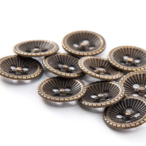 May include: A collection of antique bronze-colored buttons. Each button has a ridged design radiating from the center, with a small hole for sewing. The buttons are round and have a vintage aesthetic.