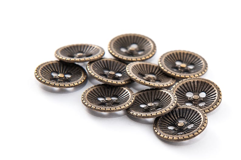 May include: A collection of antique bronze-colored buttons. Each button has a ridged design radiating from the center, with a small hole for sewing. The buttons are round and have a vintage aesthetic.