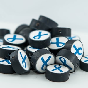 以下が含まれることがあります： 青いリボン模様の黒と白の丸いビーズの山。ビーズは中央に糸を通すための穴があります。