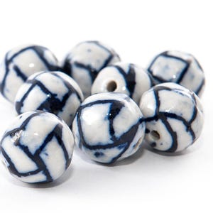 May include: A group of white ceramic beads with a dark blue geometric design. The beads are spherical and have a shiny surface, suitable for jewellery making or other crafts.