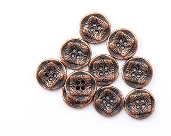 Puede incluir: Un conjunto de botones de color bronce antiguo con un diseño de cuatro agujeros. Los botones tienen un patrón texturizado, similar a una flor, en el centro y un borde oscuro. Estos botones decorativos son ideales para coser y proyectos de manualidades.