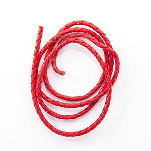 May include: Coiled red braided leather cord against a white background. The cord is tightly woven, with a visible texture. The bright red color is consistent throughout the cord, which appears to be new and unused.