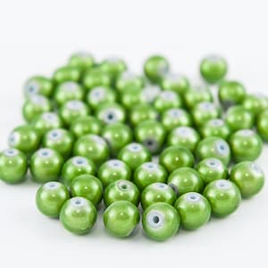 Puede incluir: Un montón grande de cuentas de vidrio verde con un centro blanco. Las cuentas son brillantes y tienen un acabado nacarado.