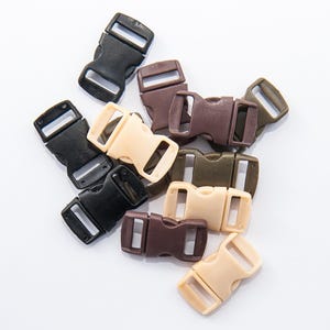 May include: A collection of plastic side-release buckles in various colors, including black, tan, brown, and olive green. These buckles are designed for use in straps and closures, and are shown against a white background.