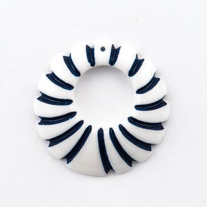 Puede incluir: Anillo de cerámica blanca con un diseño de rayas azules y blancas. El anillo tiene un agujero en el centro.