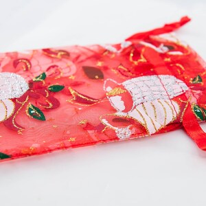May include: Red sheer gift bag with a gold and white floral design. The bag has a drawstring closure.