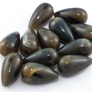 Può includere: Un gruppo di 10 perline a forma di lacrima con un motivo marmoreo marrone scuro e nero. Le perline sono in vetro o plastica e hanno una finitura lucida.