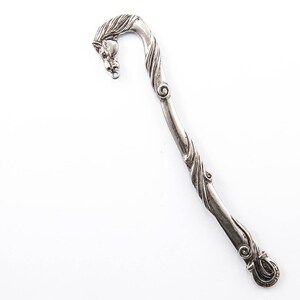 May include: A silver-toned metal bookmark with a horse head design. The bookmark has a curved shape with a detailed horse head at the top and a decorative swirl pattern along the stem. The bottom of the bookmark has a looped design.
