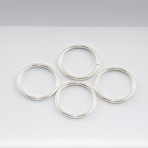 May include: Four silver jump rings, each with a circular shape, are arranged in a cross pattern on a white surface.