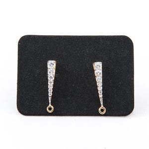 May include: A pair of elegant earrings with a triangular design. Each earring features a gold-colored base and is adorned with multiple clear, sparkling stones. The earrings are displayed on a black, rectangular surface against a white background.
