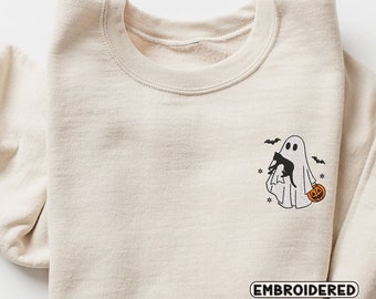 May include: A beige sweatshirt with an embroidered design of a ghost holding a black cat and a pumpkin. The text "EMBROIDERED" is below the design.