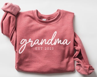 May include: A pink sweatshirt with the text "grandma est 2023" in white.