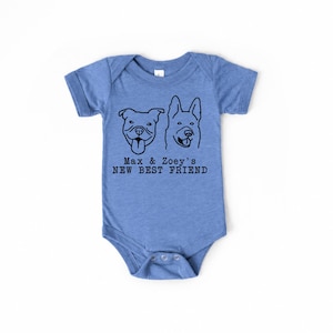 May include: A heather blue short-sleeve baby bodysuit featuring a black line art graphic of two dog faces. Below the dogs, the text reads: Max & Zoey's NEW BEST FRIEND. The garment has a crew neckline and a snap closure at the bottom crotch area.