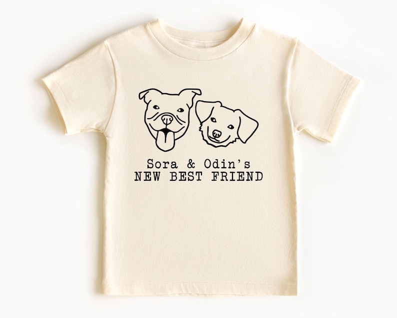 A white t-shirt with a graphic design featuring two dog faces and the text "Sora & Odin's NEW BEST FRIEND".