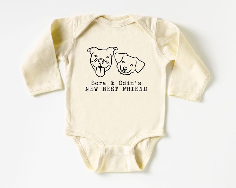 A baby onesie with a graphic of two dogs and the text "Sora & Odin's NEW BEST FRIEND" printed on it.
