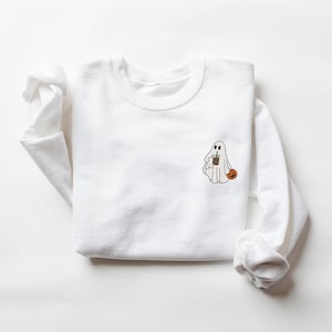 May include: White long-sleeved sweatshirt with a small embroidered design of a ghost holding a cup of coffee and a pumpkin.