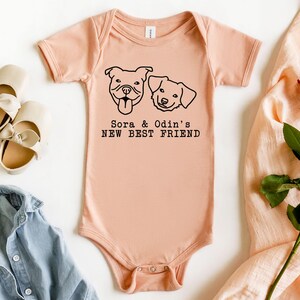 a baby onesie with a graphic of two dogs, a pink onesie, a pair of white shoes, a red rose, and a denim shirt, all arranged on a white background.