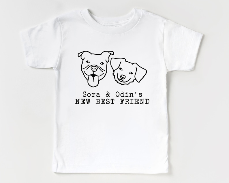 A white t-shirt with a graphic design featuring two dog faces and the text "Sora & Odin's NEW BEST FRIEND".