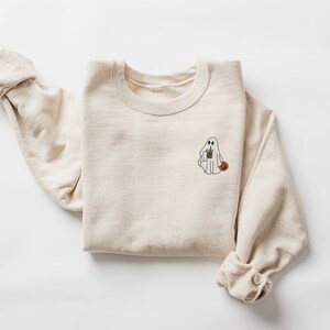 May include: A beige sweatshirt with a white ghost holding a cup and a pumpkin on the front.