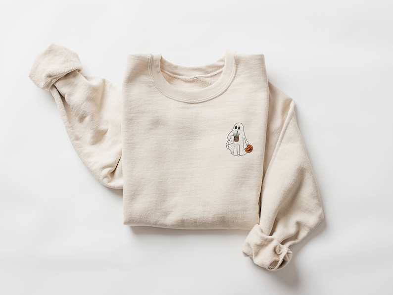 May include: A beige sweatshirt with a white ghost holding a cup and a pumpkin on the front.