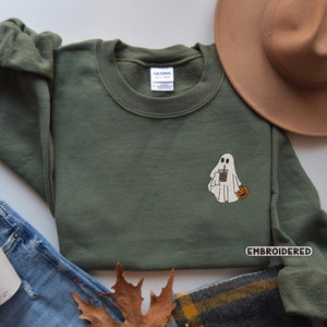 May include: A green sweatshirt with an embroidered ghost holding a cup of coffee and a small pumpkin. The text "EMBROIDERED" is on the bottom right corner of the sweatshirt.