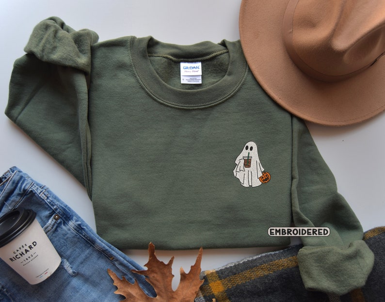 May include: A green sweatshirt with an embroidered ghost holding a cup of coffee and a small pumpkin. The text "EMBROIDERED" is on the bottom right corner of the sweatshirt.