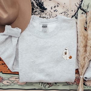 May include: A gray sweatshirt with a white ghost holding a cup of coffee and a small pumpkin. The ghost is wearing a white sheet and has a friendly face.
