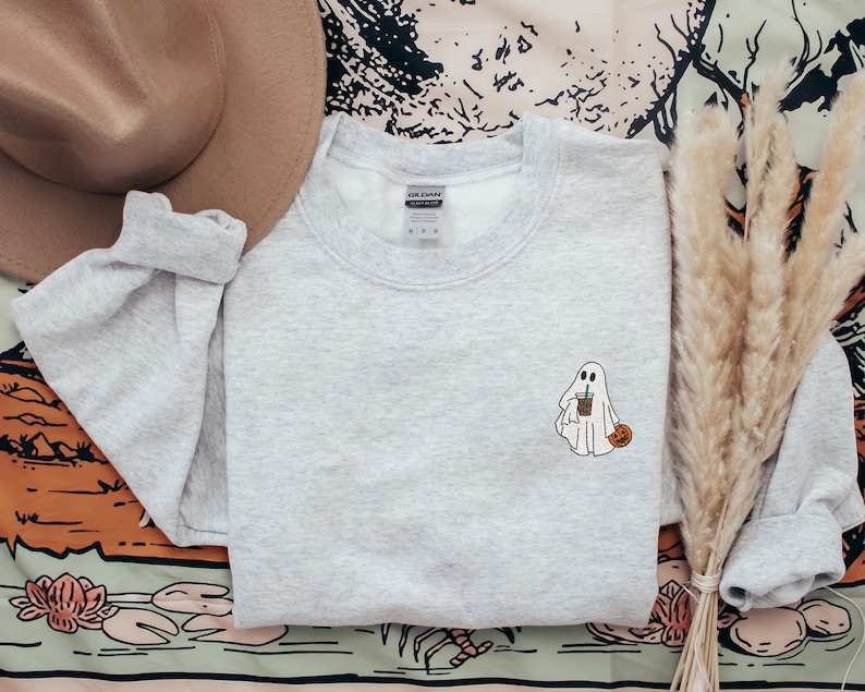 May include: A gray sweatshirt with a white ghost holding a cup of coffee and a small pumpkin. The ghost is wearing a white sheet and has a friendly face.