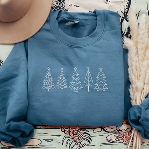 May include: A blue sweatshirt with a white embroidered design of five stylised Christmas trees. The trees are arranged in a row across the front of the sweatshirt.