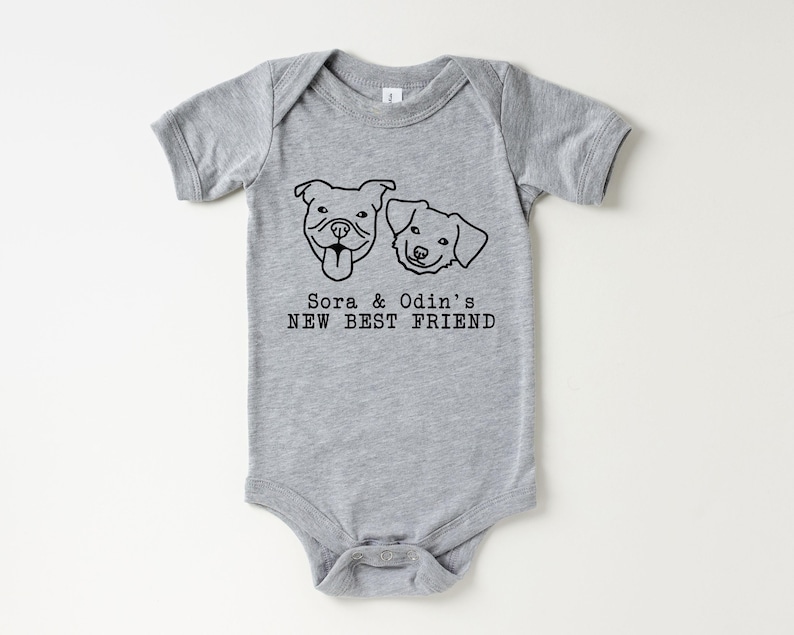 A gray baby onesie with a graphic design of two dog faces and the text "Sora & Odin's NEW BEST FRIEND" printed on it.