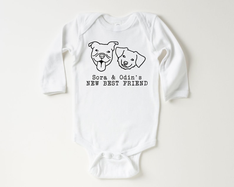 A white baby onesie with a graphic design of two dog faces and the text "Sora & Odin's NEW BEST FRIEND" printed on it.