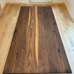 May include: A rectangular wooden table with a dark brown finish and a lighter brown central stripe. The table is made of solid wood and has a natural grain pattern. The table is approximately 183 cm long.