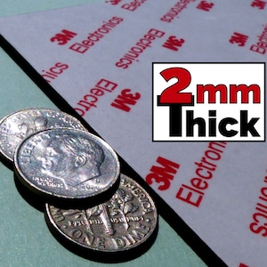 Pode incluir: Uma folha de material adesivo branco com texto da marca 3M Electronics em vermelho e um gr&aacute;fico retangular indicando 2mm Thick, posicionada ao lado de tr&ecirc;s moedas de dez centavos dos EUA prateadas sobrepostas em uma superf&iacute;cie verde clara.