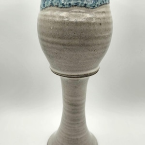 May include: A tall, white ceramic vase with a blue and brown glaze. The vase has a wide, round base and a narrow neck.